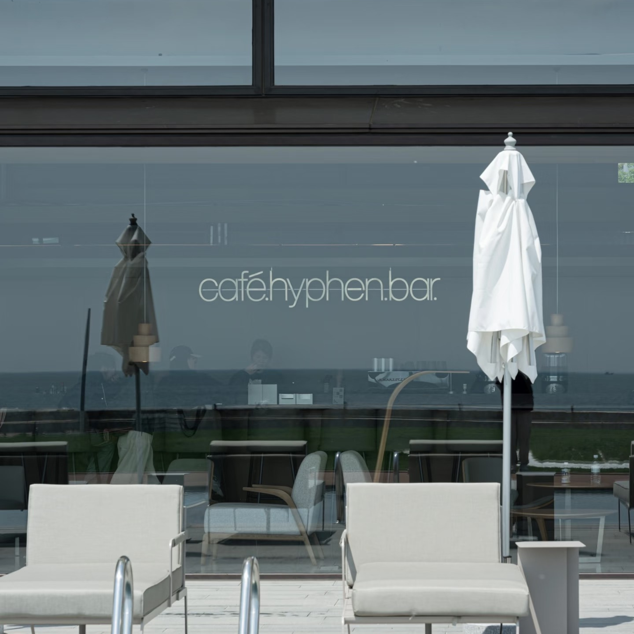 Outdoor seating area in front of a large glass window with the text 'cafe hyphen.bar' visible.