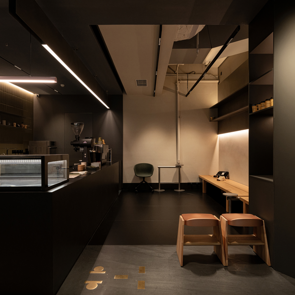 A modern, minimalist interior space with dark wood cabinetry, warm ambient lighting, and a few light wood chairs and a small table in a cafe-like setting.