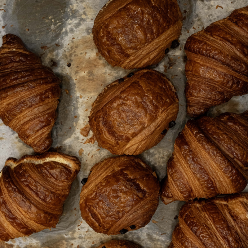 Several golden-brown baked croissants arranged on a rustic metal baking sheet.