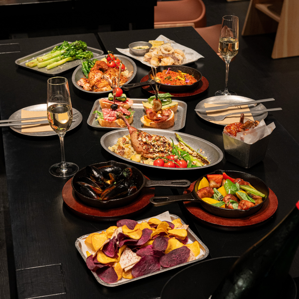 A dining table set with multiple plates of prepared food, including shrimp, pasta, vegetables, chips, and wine glasses, in a restaurant setting.