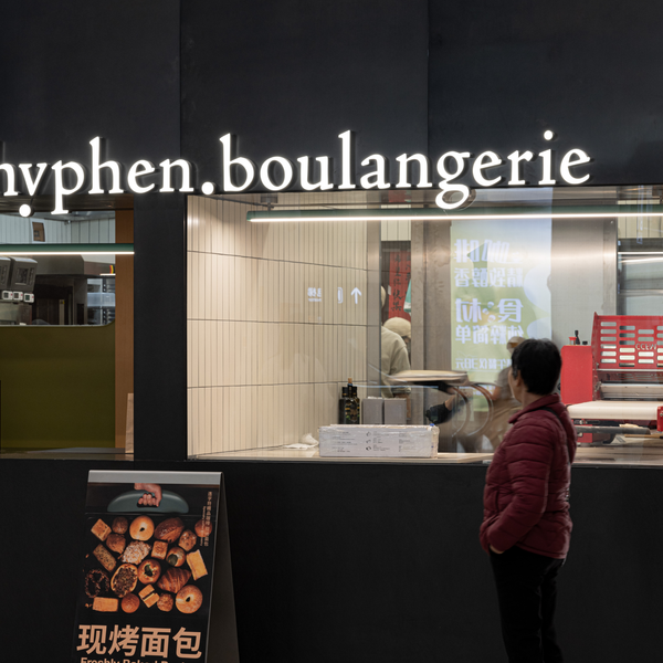 A person in a red puffer jacket stands in front of a bakery storefront with the sign 'hyphen.boulangerie' visible.